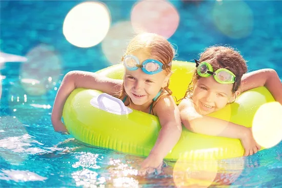 Zwei Kinder mit Schwimmbrillen auf einer Luftmatratze im Pool