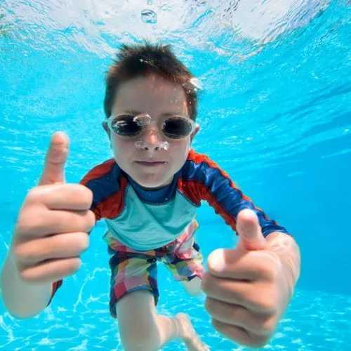 Kind mit Schwimmbrille gibt unter Wasser den Daumen hoch