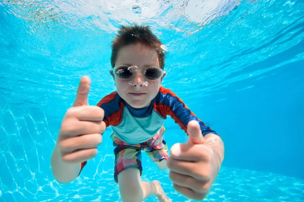 Kind mit Schwimmbrille gibt unter Wasser den Daumen hoch