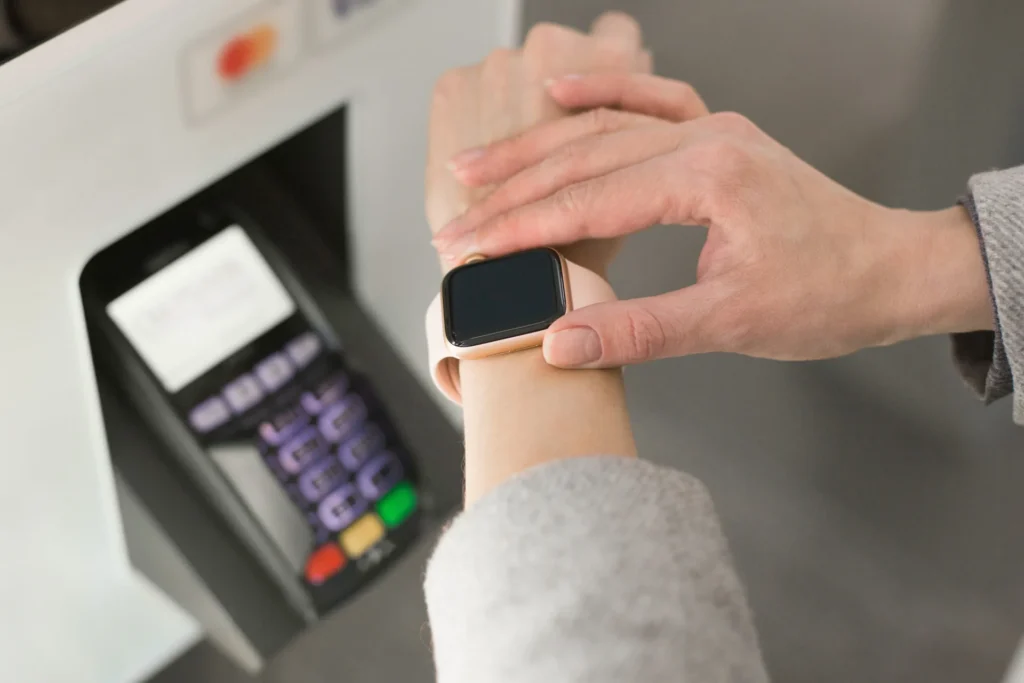 Hand hält eine Smartwatch vor einem kontaktlosen Terminal