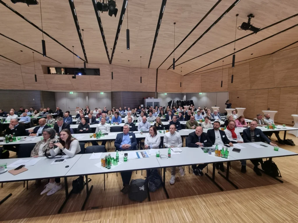 Konferenzteilnehmende an langen Tischen in einem modernen Saal