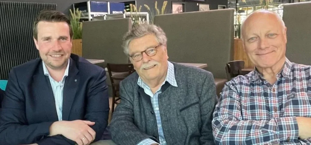 Drei Männer sitzen nebeneinander an einem Tisch